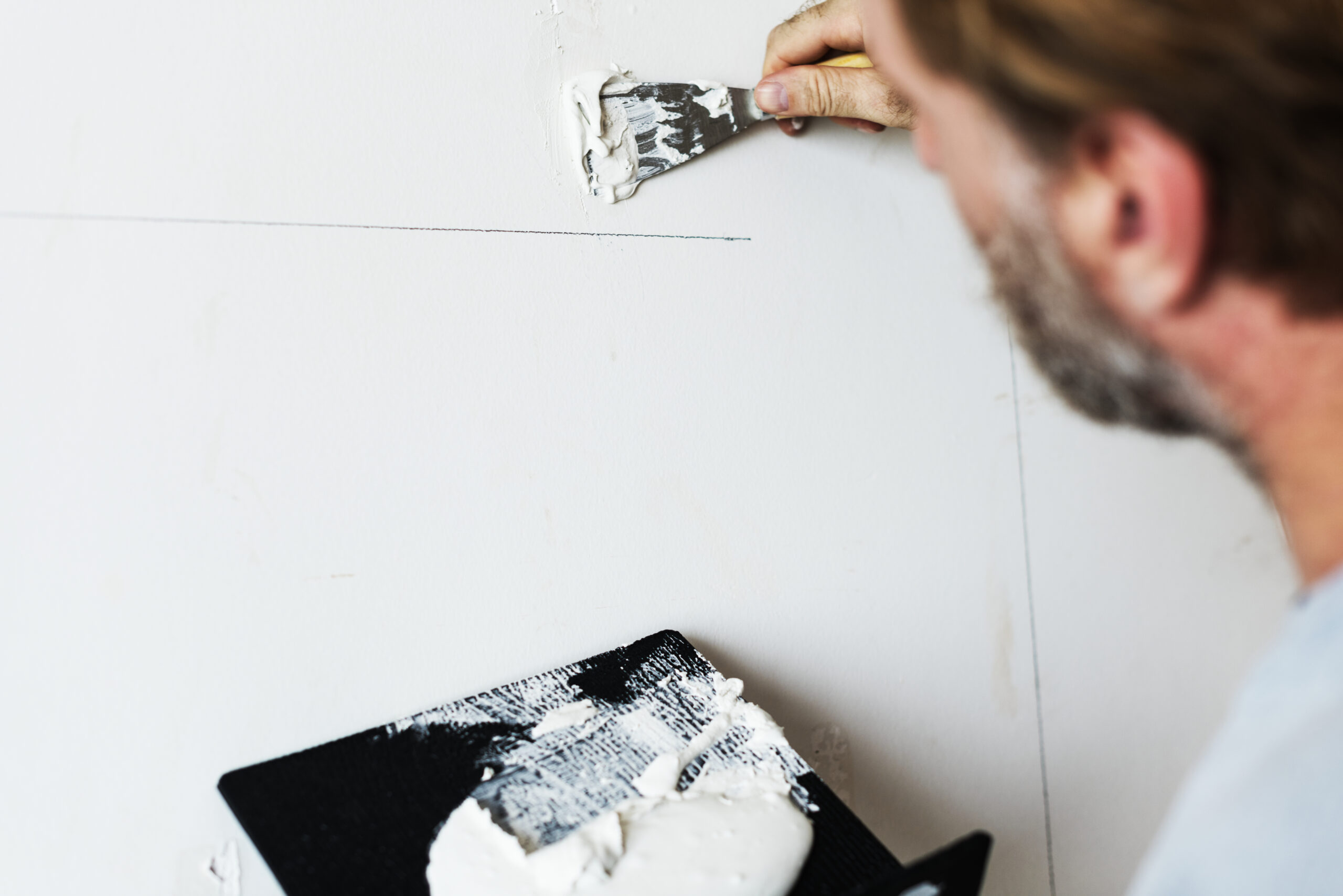 Worker applying drywall patch with a putty knife to fix a wall